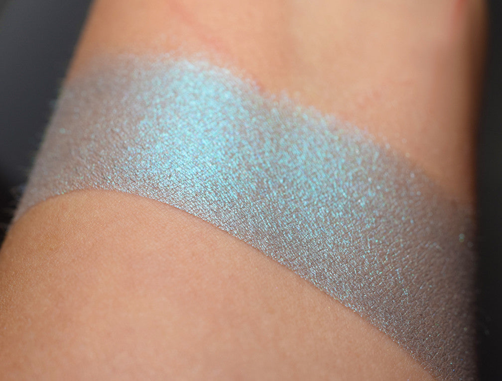 AMERAUCANA eyeshadow shown in several views: loose, and swatched on the skin. A pale/medium heathered grey blue with a strong teal/blue shift.