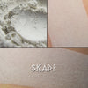 Skadi pure white matte eyeshadow shown loose and swatched on the skin.