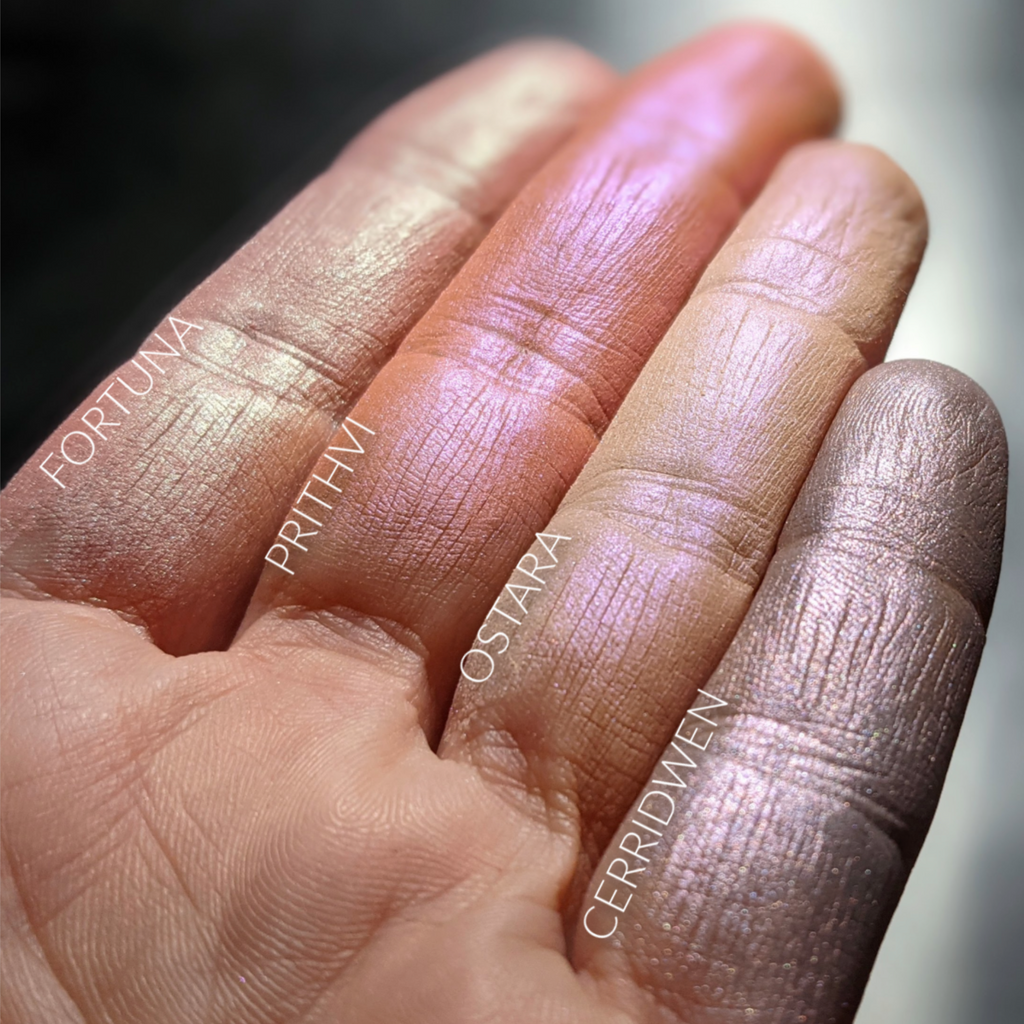 Pale, iridescent finger swatches of different glowing cheek products. Cerridwen is a unique shade with tones of silvery pink and mauve. 