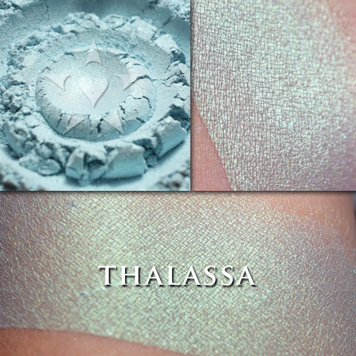 Thalassa highlighter loose and swatched on the skin. This glowy mermaid-like highlighter is a pale teal with strong green to gold iridescence
