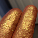 Image showing closeup fingertip swatches at an angle with very vivid gold highlight against a deep burnt red background.