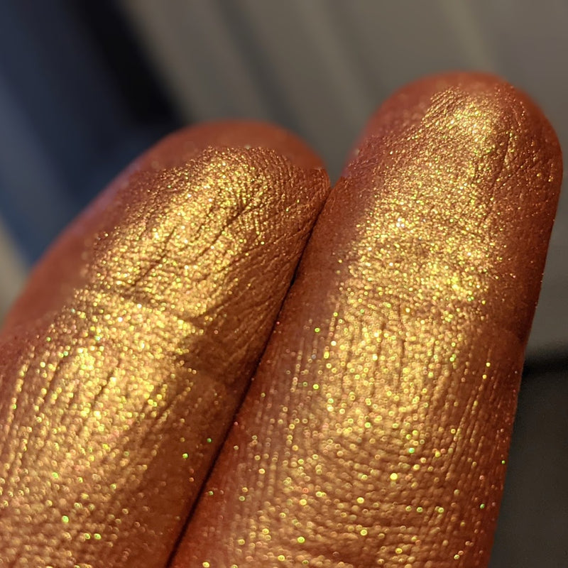 Image showing closeup fingertip swatches at an angle with very vivid gold highlight against a deep burnt red background.