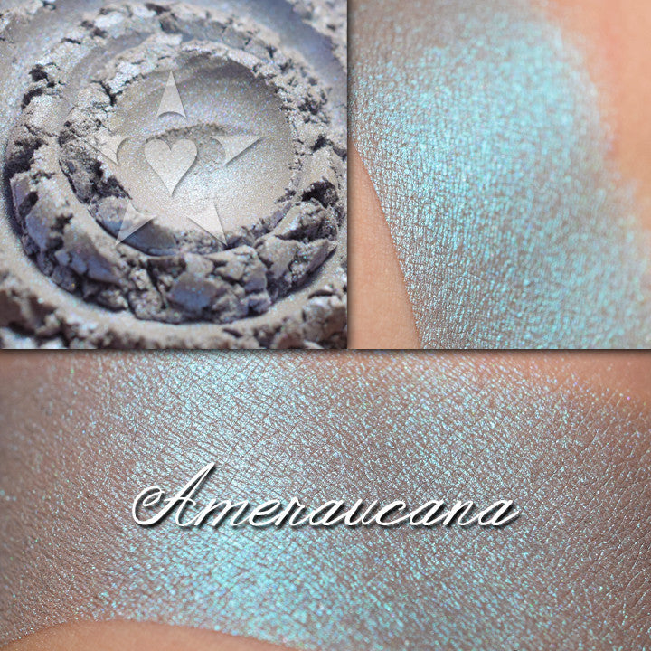 AMERAUCANA eyeshadow shown in several views: loose, and swatched on the skin. A pale/medium heathered grey blue with a strong teal/blue shift.
