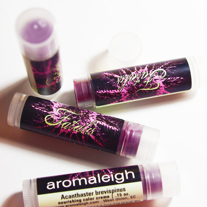 Image shows tubes of lip product. Tubes are clear plastic, with black, purple and green labels.
