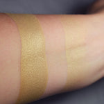 Automeris swatched on medium tone caucasian skin over a primer, and on bare skin. A pale buttery cream/gold.