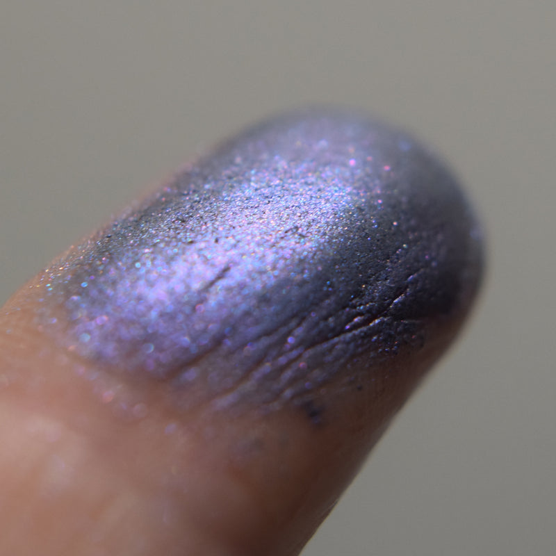 Adelaide eyeshadow shown close up and shimmering on a fingertip. Image of swatches on skin of Adelaide eyeshadow. Adelaide is a rich violet-blue with multi-tonal overlays of rose and violet.