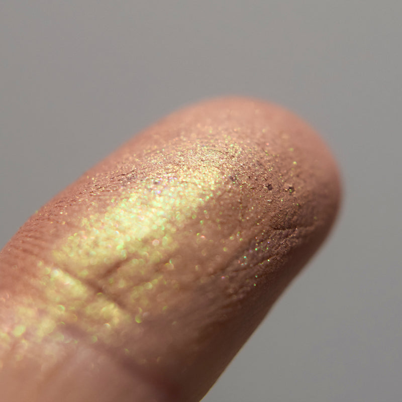Image shows a closeup of Agnodice eyeshadow on a fingertip. You can see the strong iridescent gold to green.