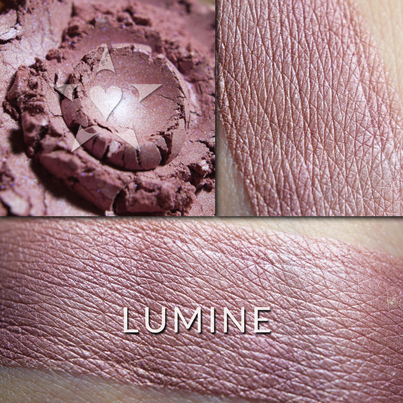 Lumine multi purpose illuminator loose and swatched on the skin. LUMINE: A deeper-toned, rosy plum with a soft blue iridescence.'