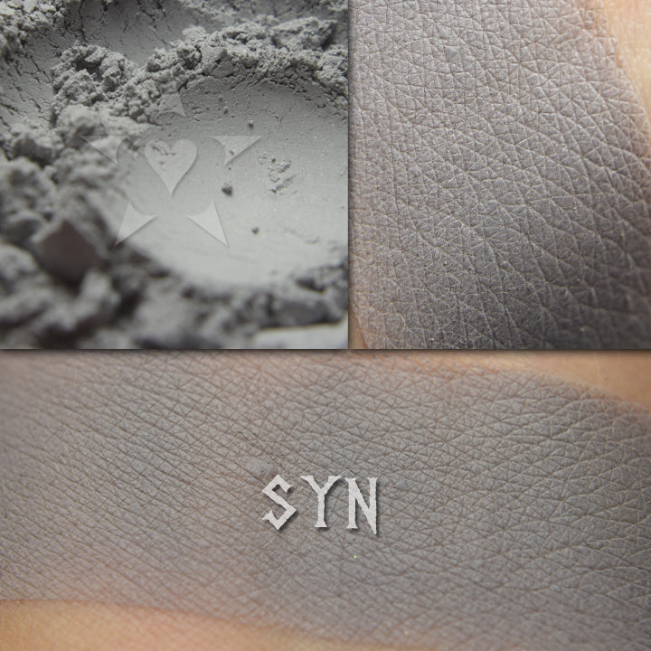 Syn matte eyeshadow shown loose and swatched on the skin. Soft grey with cool undertones.