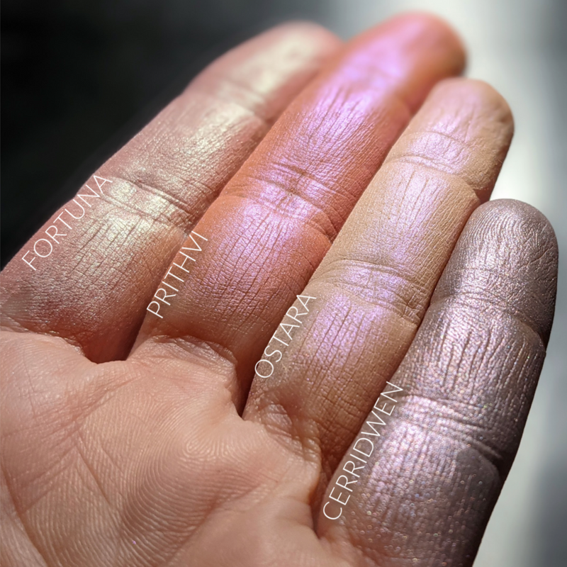 Pastel toned iridescent highlighters and rouge swatched on the fingertips. Ostara is a soft peach with a strong purple highlight. 