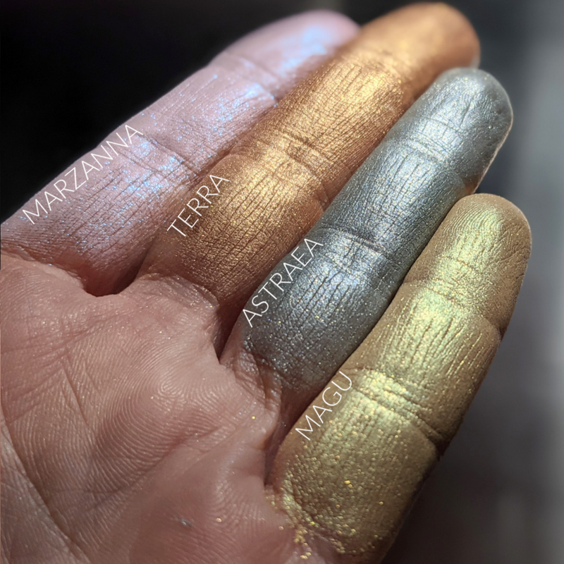 Finger swatches of different pale toned highlighters. Astraea is second from the right. soft blue-grey toned highlight powder with a celestial gold shift and shimmer