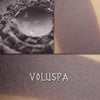 Voluspa matte eyeshadow shown loose and swatched on the skin. Medium-deep gray with strong violet/mauve tones.