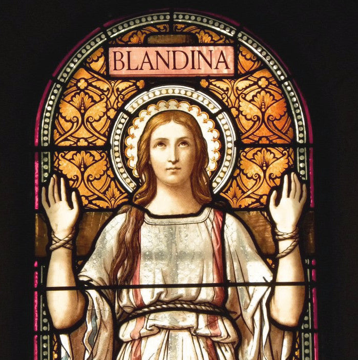 Stained glass window showing St. Blandina in white robes with hands facing upward. She has rope around her waist and wrists.