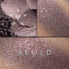 SKULD eyeshadow loose and swatched on the skin. Skuld has iridescent effects of red to violet, and copper tones, within a base of weathered red with dark violet undertones.